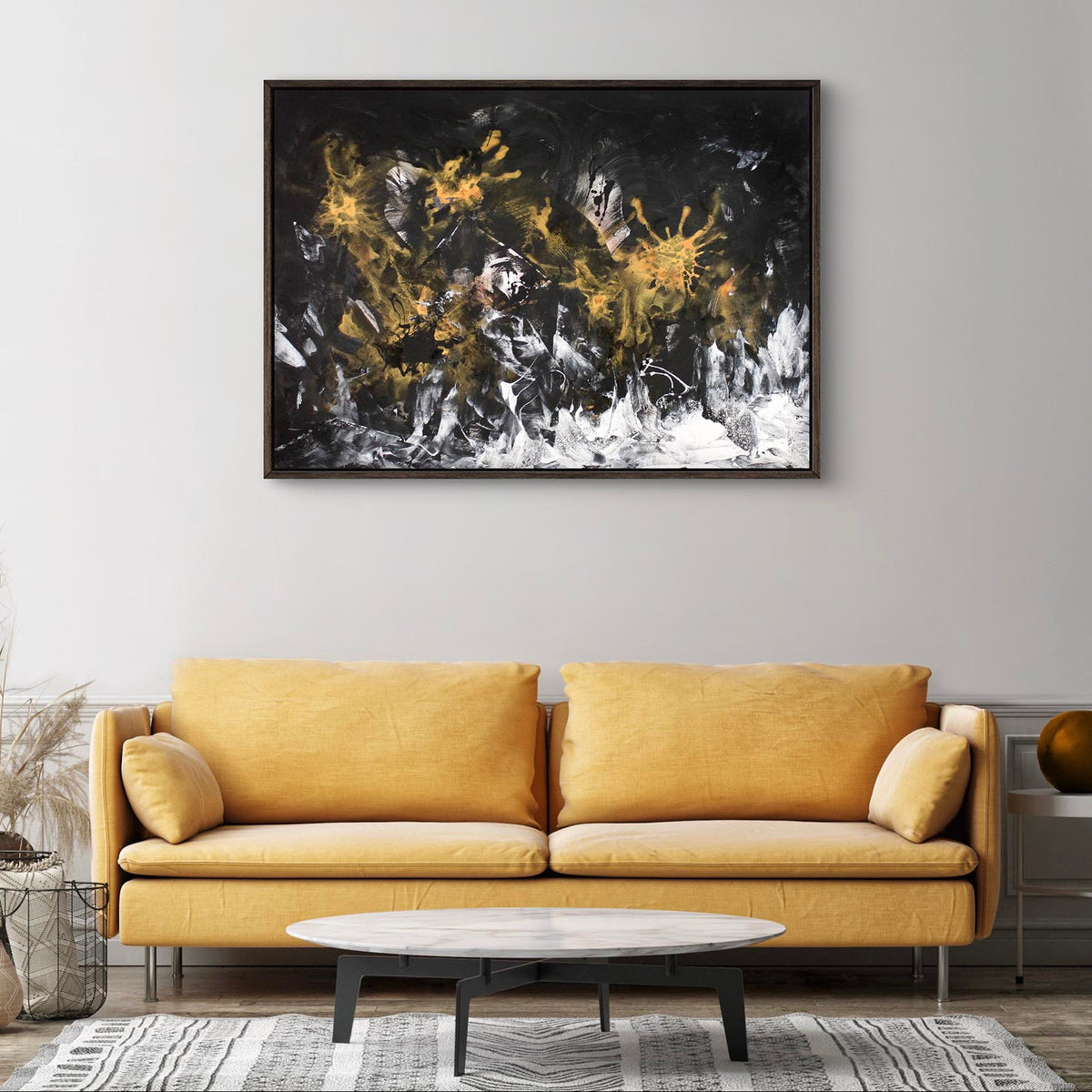 Framed abstract landscape painting featuring dramatic black, white, and gold brushstrokes on a dark background, displayed on a wall above a yellow sofa in a modern living room setting.
