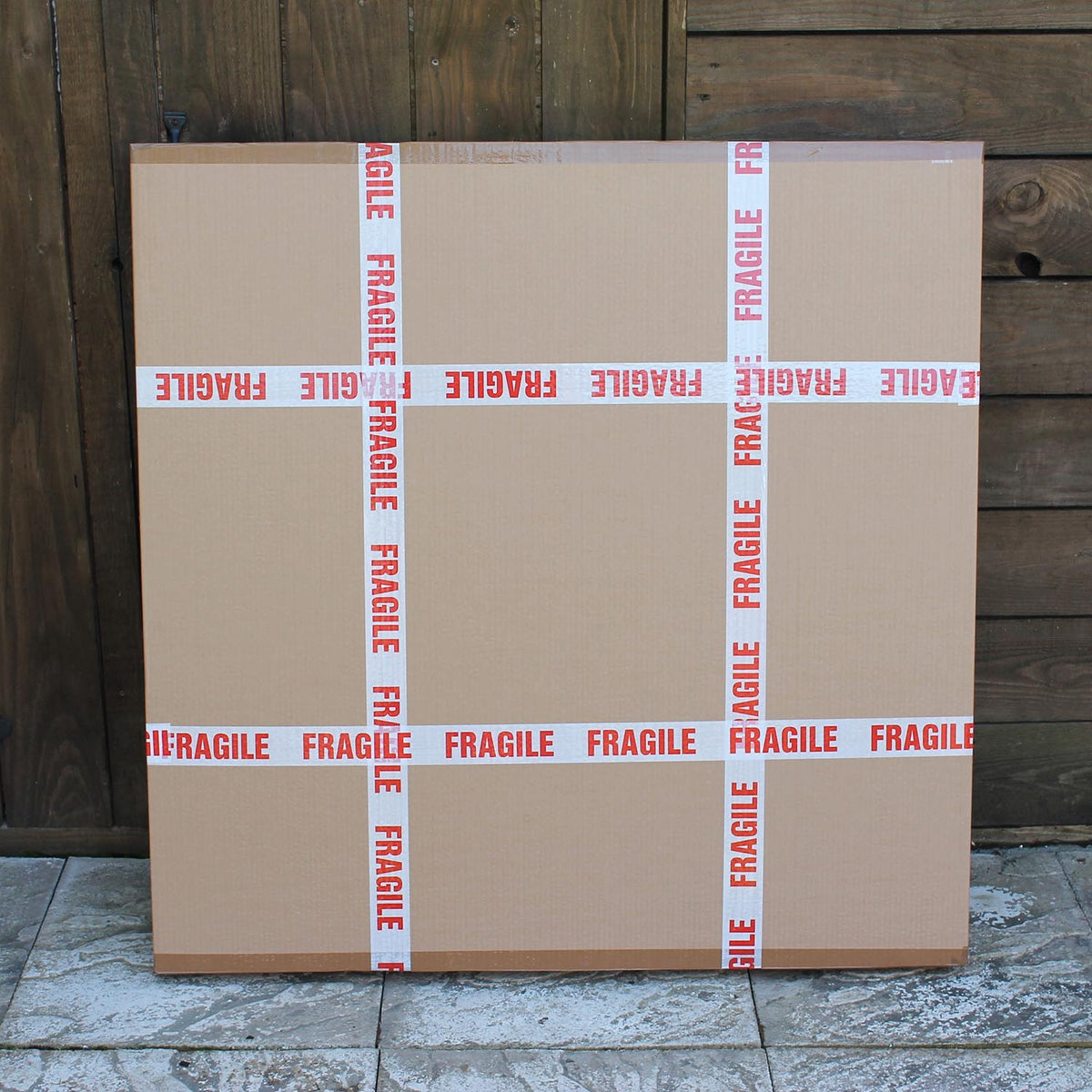 Large fragile cardboard boxes stacked on a wooden surface against a wooden wall background.