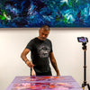 Talented abstract artist painting large colorful canvas in front of a vivid, textured artwork hanging on the wall