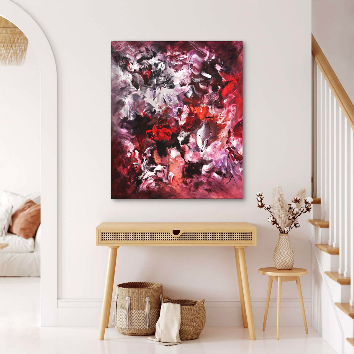 Large abstract canvas art depicting a vibrant, colorful floral landscape in purple, red, and white hues. The painting is displayed on a white wall in a minimalist, modern interior setting with wooden furniture accents.