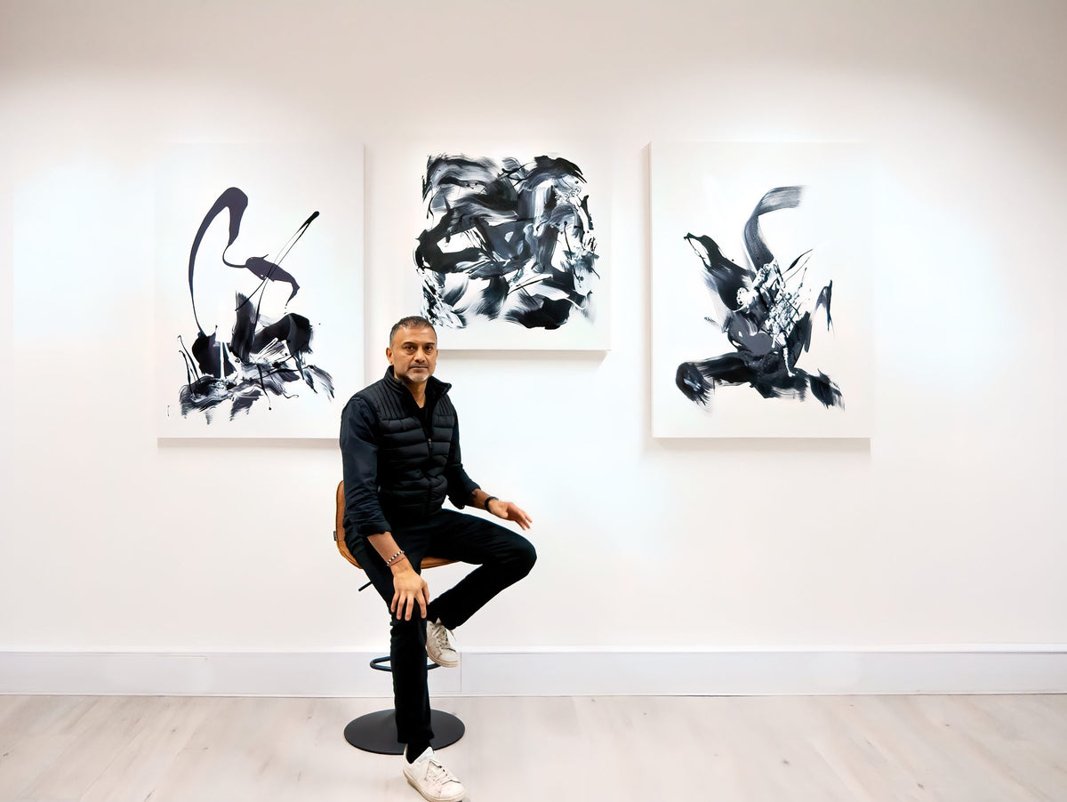 Paresh Nrshinga FRSA seated in front of three original black and white gestural abstract paintings