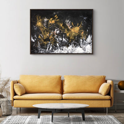 Framed abstract landscape painting featuring dramatic black, white, and gold brushstrokes on a dark background, displayed on a wall above a yellow sofa in a modern living room setting.